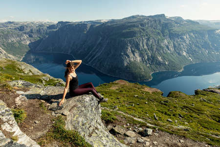 A young and beautiful woman poses on the rock overviewing Ringedalsvatnet Lake in Odda, , Vestland county, Norwayの写真素材