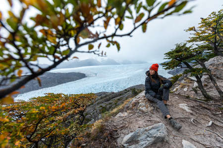 A young woman sits on the rock with Grey Glacier on the background, Torres del Paine National Park, Chileの写真素材