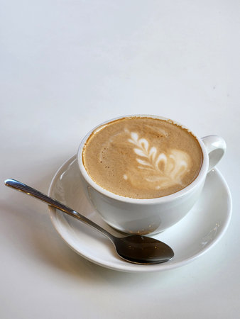 Coffee in a white cup on a white table. Cup and spoon