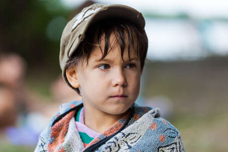 Cute boy sitting wrapped in a warm towel after having fun in the riverの写真素材