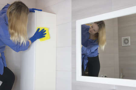 Young girl dusting furniture with a rag in the bathroomの写真素材