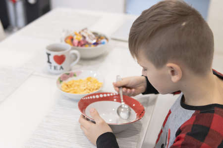 Child having breakfast. Kid drinking milk and eating cereal with fruit. Little boy at white dining table in kitchen. Kids eat on sunny morning. Healthy balanced nutrition for young kids.の写真素材