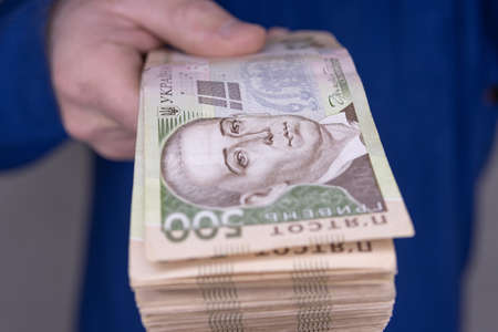 A man in a blue sweater holds a stack of new banknotes of the Ukrainian hryvnia in his hands 500...