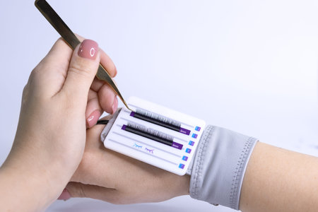 female hand holds eyelash extension tweezers and takes eyelashes, black eyelashes are glued on a...