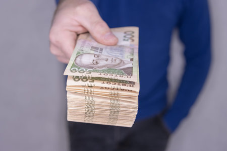man in a blue sweater holds a stack of new banknotes 500 hryvnia.
