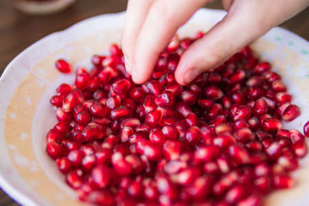childs hand takes a red pomegranate from a plate close-upの写真素材