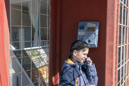 boy of European appearance in telephone booth is talking on the phone