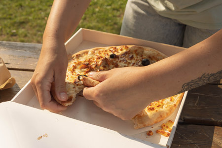 a girl with a tattoo on her arm in the shape of a wing breaks pizza at a picnic in the parkの写真素材