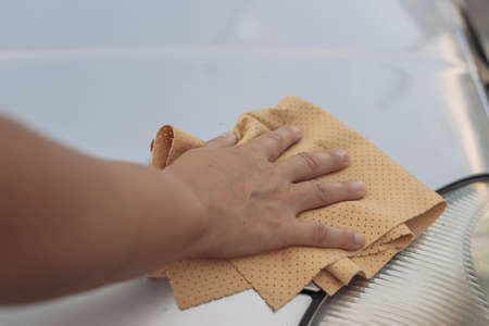 The girl wipes the window in the car with a yellow special cloth for windows.Close-up of a hand and a rag.there is a place for an inscription. The concept of work and cleanlinessの写真素材