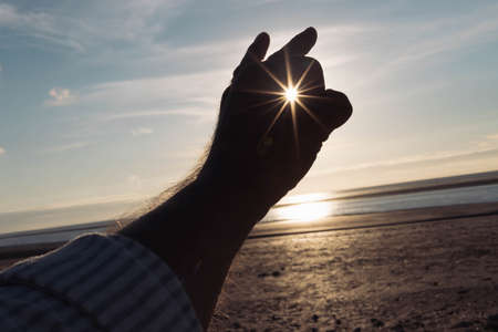 a mans hand is isolated against the background of the sky, A beautiful landscape, is a place for an inscription. A mans hand against the background of a sunset in his fingers holds a small sun.の写真素材
