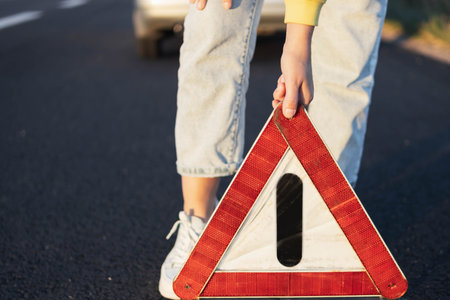 a girl puts an emergency stop sign on the highway near a broken car close-up on the sign. A car...