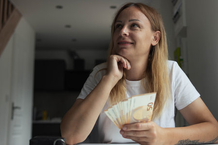 a girl in a white t-shirt sits indoors at a white table with her hands folded and is thoughtful...