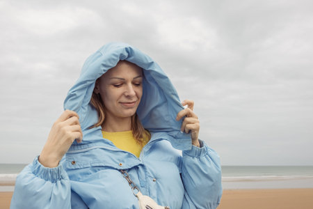 a girl of European appearance with blond hair stands on the seashore in a blue jacket and smiles...
