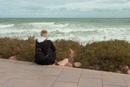 The girl sits on the embankment and looks at the sea. the girl sits with her back to the cameraの写真素材