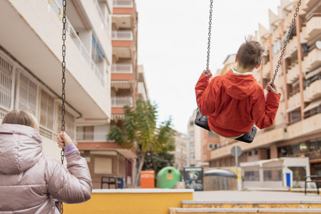 two children ride on a swing with their backs to the camera there is a place for an inscriptionの写真素材