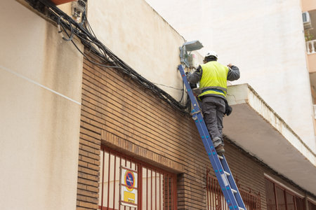 a man in work clothes, turned with his back to the camera, makes wiring on a stepladder. There is a place for an inscriptionの写真素材