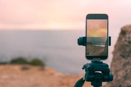 beautiful seascape has a place for an inscription close-up on the phone,smartphone camera stands on a tripod close-up, photographing a picturesque evening sunset over a tropical sea and a mountain.の写真素材