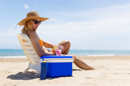 Happy young european girl drinks a cocktail and rests in a sun lounger on the beach,の写真素材