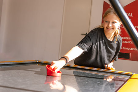 Cute teen girl plays air hockey arcade in game machine at an amusement park.