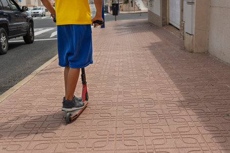 a child in casual clothes rides a scooter on the street, with his back turned to the camera,