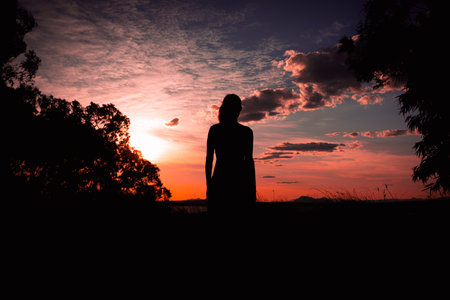 silhouette of a sports girl in a dress in nature the girl looks at the sunset concept of freedomの写真素材