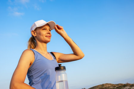a girl in sportswear in a white cap and a blue T-shirt stands against the blue sky,の写真素材