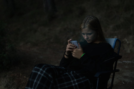a teenage girl in casual clothes sits on a chair in a Camping and looks at the phone,の写真素材