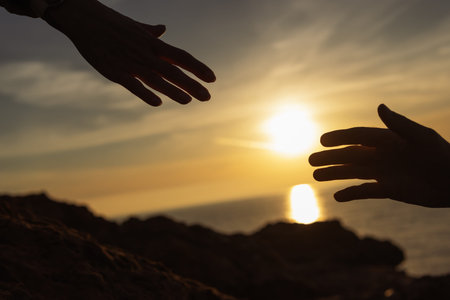 Human hands reaching out for help, support, and connection, silhouetted against a golden ocean sunset, embodying concepts of hope, teamwork, and assistance in a challenging environment