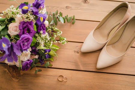 on a wooden table a wedding bouquet with green leaves, purple and white flowers, wedding rings. top view. close upの写真素材