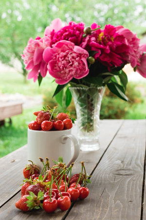 A white cup with fresh berries: cherries, strawberries, blueberries and raspberries, with more...