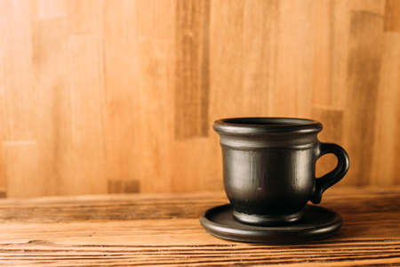 Black clay mug with coffee on a white background. a clay cup of black color on a wooden table. Close up. side viewの写真素材