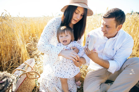 Happy childhood, family walking on the wheat field. Mother, father and little daughter leisures together outdoor. Parents and kid playing on summer meadowの写真素材