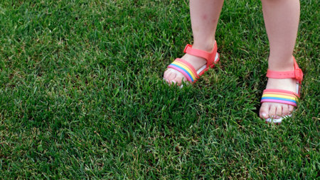 childrens legs in sandals with a rainbow on the grassの写真素材