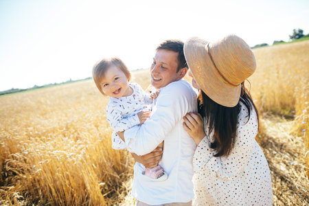 Happy family on a summer walk, mother, father and child walk in the wheat field and enjoy the beautiful nature, at sunsetの写真素材