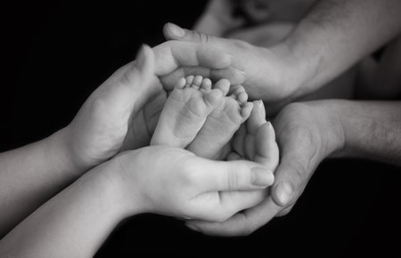 the legs of the child in the arms of the mother and the father the legs of a newborn baby . black and white photoの写真素材