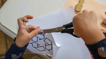 Little toddler girl cuts out a garbage sorting sign with scissors