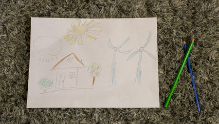 A childs drawing of a house with trees next to windmills lies on a gray carpet. Ecology concept