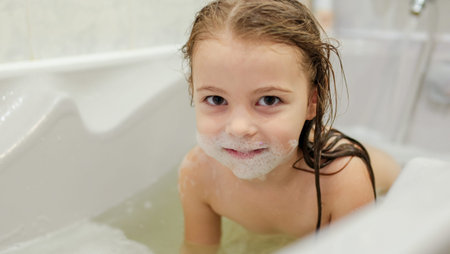 A small, smiling, beautiful red-haired girl with long hair, the child bathes, washes her face and...
