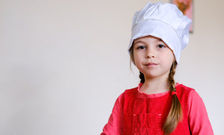 Little Caucasian girl, wearing a chefs hat, playing at being a cook in her little toy kitchen.の写真素材