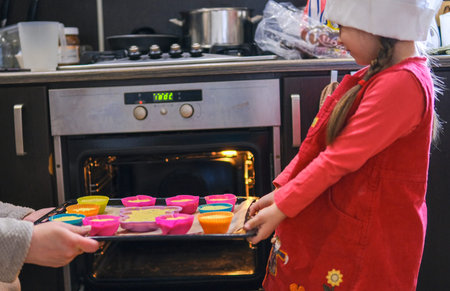 Beautiful little girl and her mother in beige aprons, showing rolled dough in the molds, while...