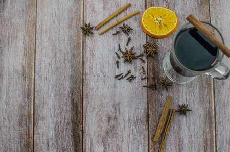 Hot mulled wine drink with lemon, apple, cinnamon, anise and other spices in a glass cup between fir tree branches on wooden cutting board. Copy spaceの写真素材