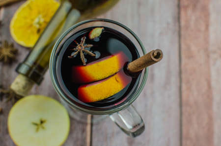 Hot mulled wine drink with lemon, apple, cinnamon, anise and other spices in a glass cup between fir tree branches on wooden cutting board. Copy spaceの写真素材