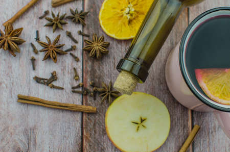 Hot mulled wine drink with lemon, apple, cinnamon, anise and other spices in a glass cup between fir tree branches on wooden cutting board. Copy spaceの写真素材
