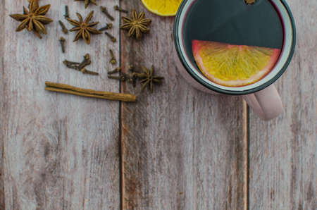 Hot mulled wine drink with lemon, apple, cinnamon, anise and other spices in a glass cup between fir tree branches on wooden cutting board. Copy spaceの写真素材