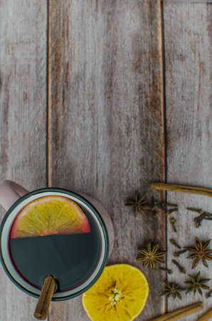 Hot mulled wine drink with lemon, apple, cinnamon, anise and other spices in a glass cup between fir tree branches on wooden cutting board. Copy spaceの写真素材