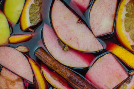 Hot mulled wine drink with lemon, apple, cinnamon, anise and other spices in a glass cup between fir tree branches on wooden cutting board. Copy spaceの写真素材