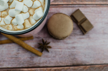 Cocoa drink with spices, zephyr and macaroons on wooden background