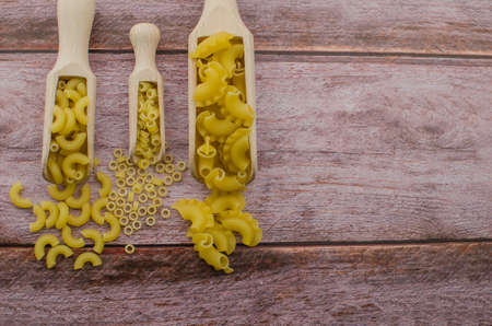 Dried pasta food selection in wooden spoons over old oak background.の写真素材