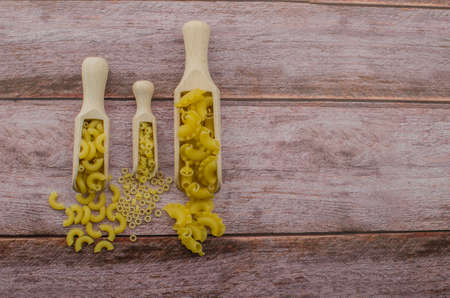 Dried pasta food selection in wooden spoons over old oak background.の写真素材