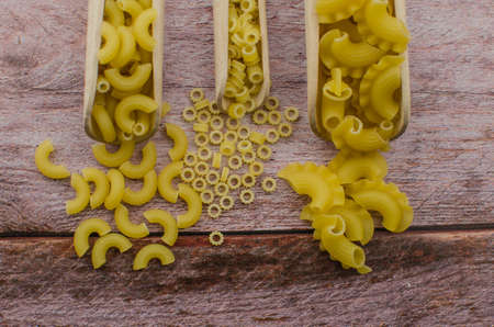 Dried pasta food selection in wooden spoons over old oak background.の写真素材